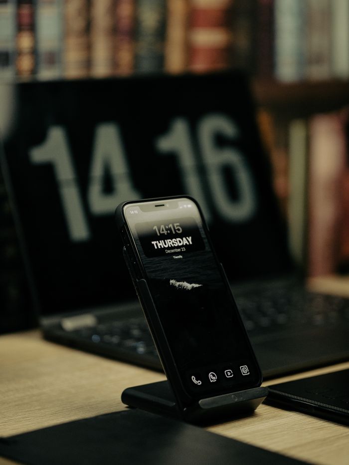 Smartphone on a wireless charger in front of a laptop displaying the time, creating a modern office vibe.