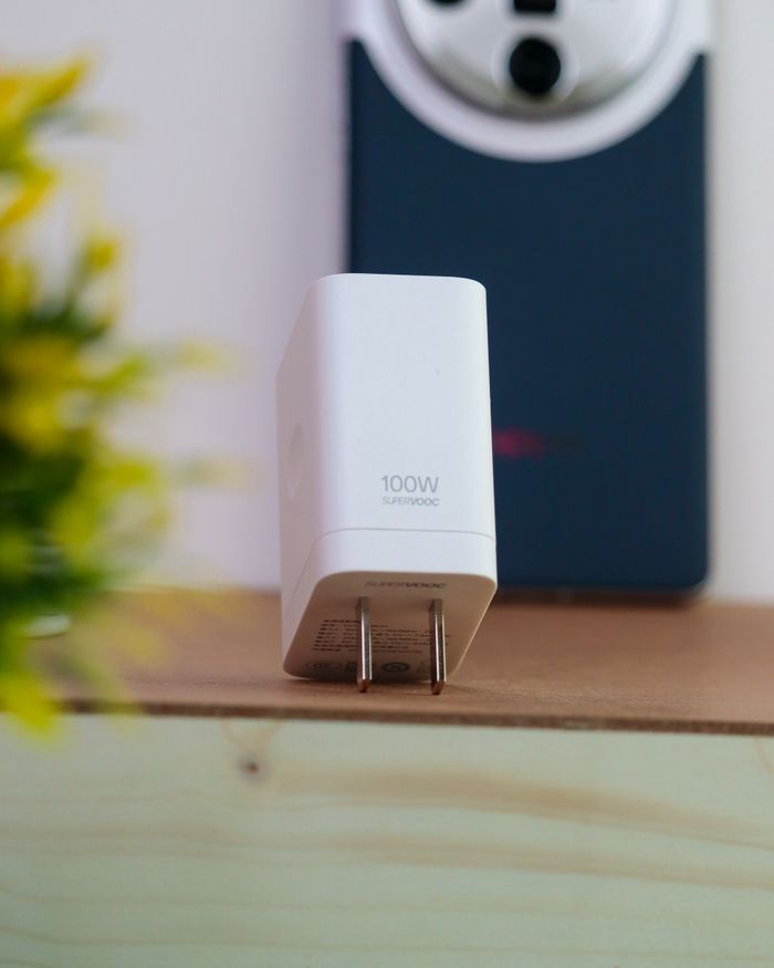 Close-up of a 100W SuperVOOC charger on a table with a smartphone in the background.