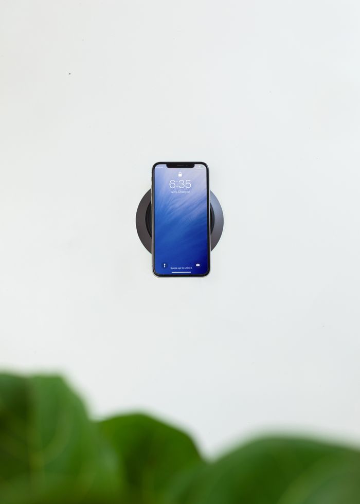 A smartphone on a wireless charger with a green leaf in the foreground, offering ample copy space.